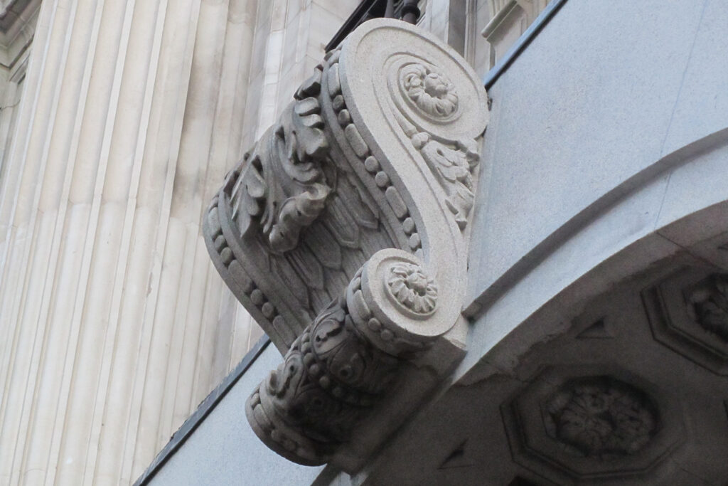 Close-up view of an ornate Ionic-style capital with scrolled volutes and carved rosette detailing at 214 Oxford Street, London, during commercial façade cleaning by Styles Façade Solutions®. The stonework shows a clear contrast between the pale, cleaned surface and the darker, grime-covered sections beneath, highlighting the intricate carved acanthus leaves and decorative moulding as the cleaning process progresses across the façade.
