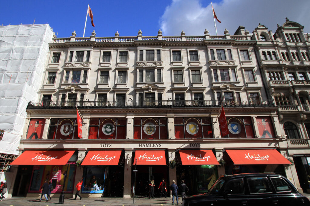 Styles Façade Solutions® reveals the striking transformation of the historic Hamleys building, London, following the Façade Gommage cleaning process, with the once-stained stonework now bright and uniformly restored, showcasing the building's original architectural detail against neighbouring scaffolded premises.
