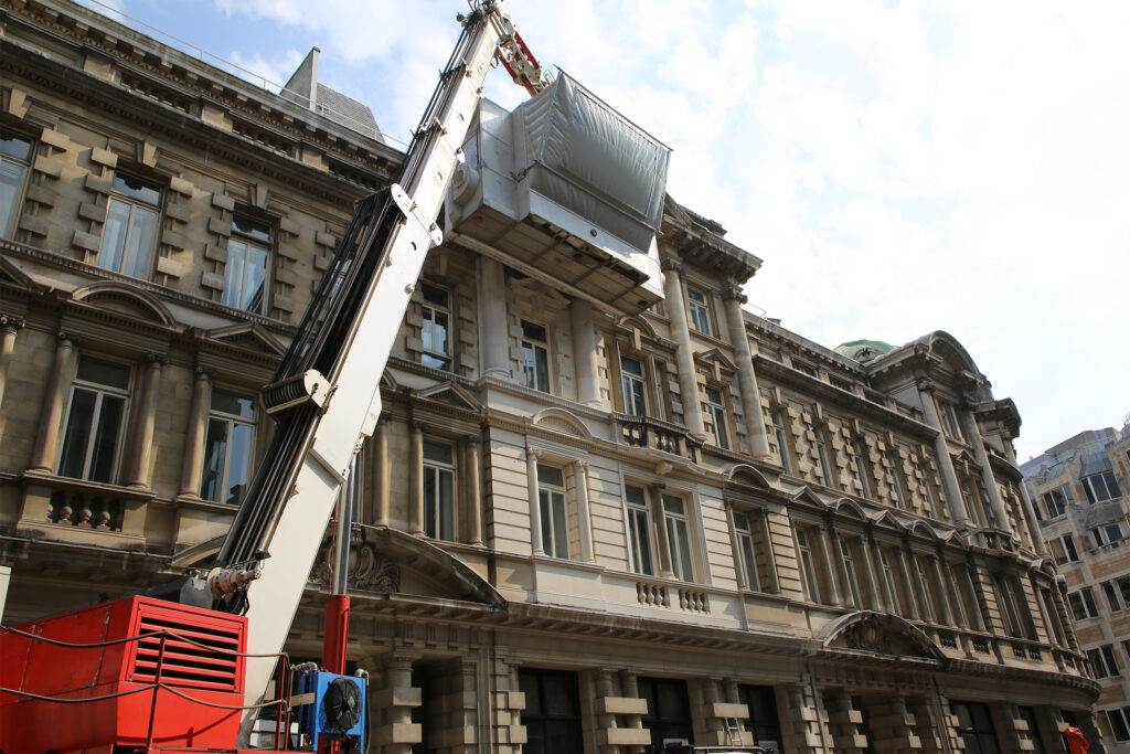 Styles Façade Solutions® prepares the Façade Gommage cleaning process at 1-5 London Wall, London, positioning a crane-mounted, enclosed access cabin against the weathered stone upper storeys, ready to restore the building's ornate classical detailing to its original bright appearance.