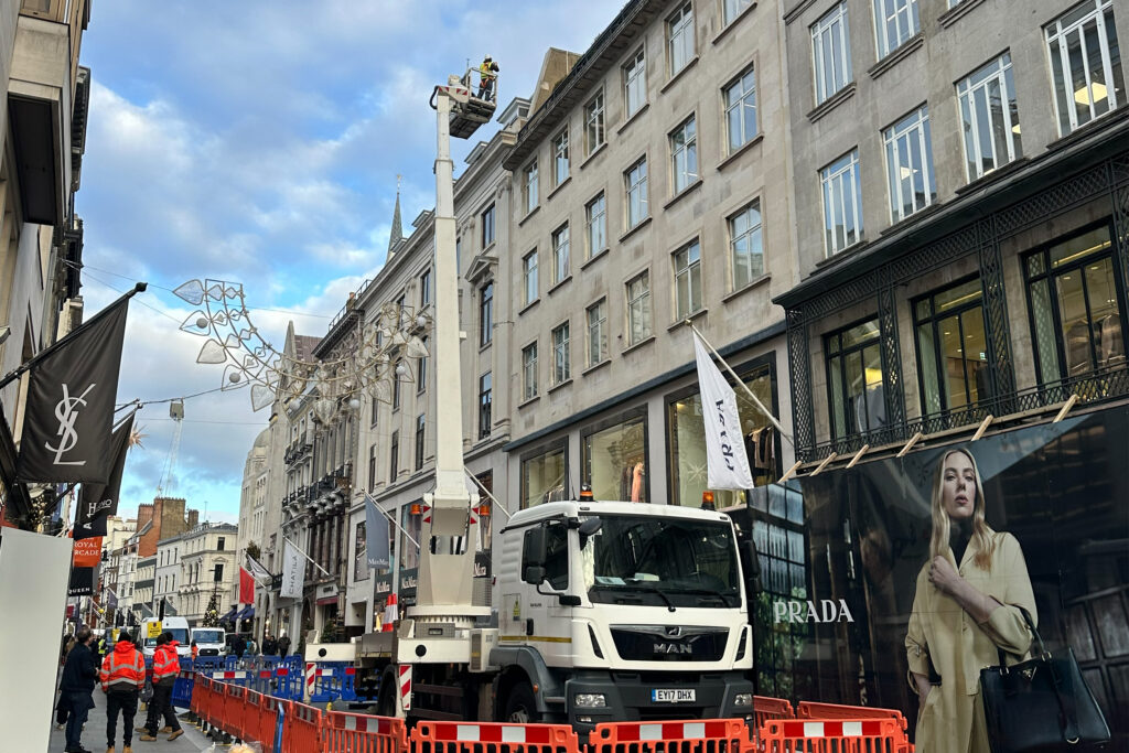 Styles Façade Solutions® extends its access platform to full height outside 16-18 Old Bond Street, London, for a comprehensive rooftop-level survey. With the truck secured behind safety barriers, the elevated inspection captures the building's full stone frontage above the surrounding luxury retail storefronts.