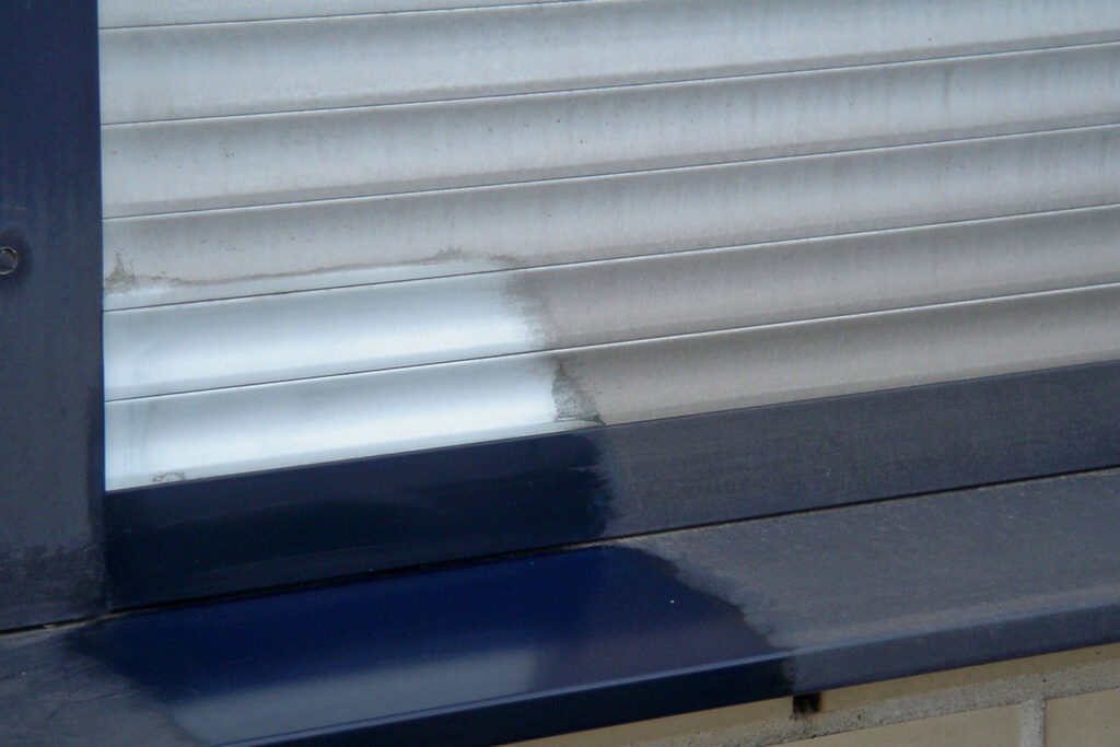 Styles Façade Solutions® cleans ribbed stainless steel and coated aluminium shutters, revealing a clear divide between weathered, streaked panels and brighter, restored sections.
