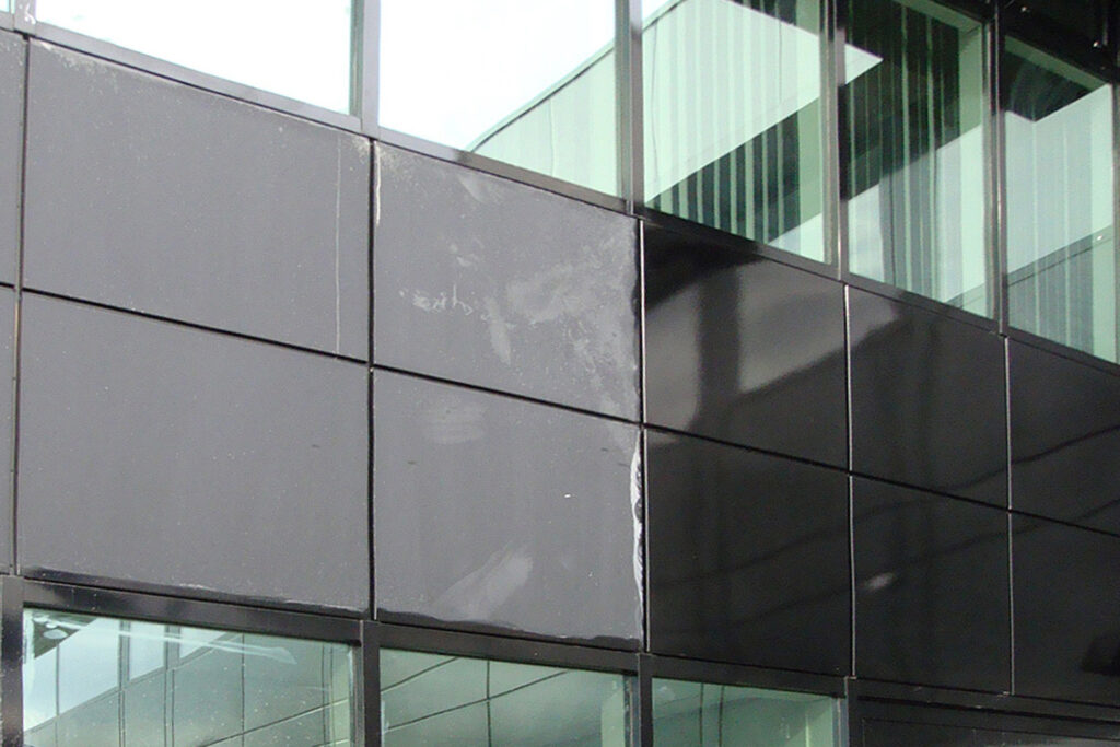 Styles Façade Solutions® recoats coloured aluminium panels, revealing a sharp contrast between weathered, faded sections and freshly applied glossy coating. The visible divide across the façade highlights the depth and richness restored to the finish, showcasing quality workmanship mid-renovation.