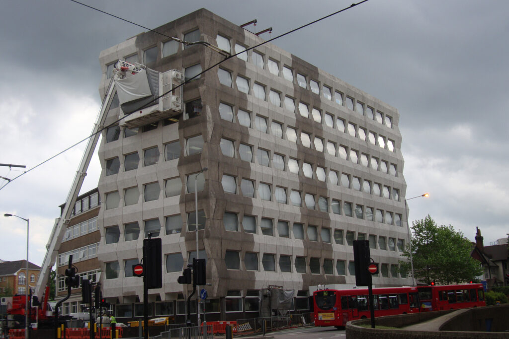 Styles Façade Solutions® cleaning the distinctive pre-formed concrete façade of Alico House, Croydon, using the Façade Gommage process. The scaffold-free specialist cleaning unit, crane-mounted at upper level, demonstrates the system's versatility in treating large-scale Brutalist concrete façades as effectively as delicate historic stonework.