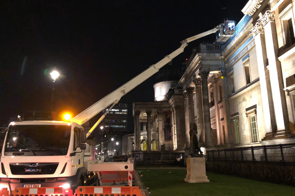 Styles Façade Solutions® conduct an overnight high-level façade survey on The National Gallery, Trafalgar Square, London. The truck-mounted boom lift extends to the building's upper cornice, positioning the team precisely against the landmark's grand Portland stone façade and Corinthian colonnade.