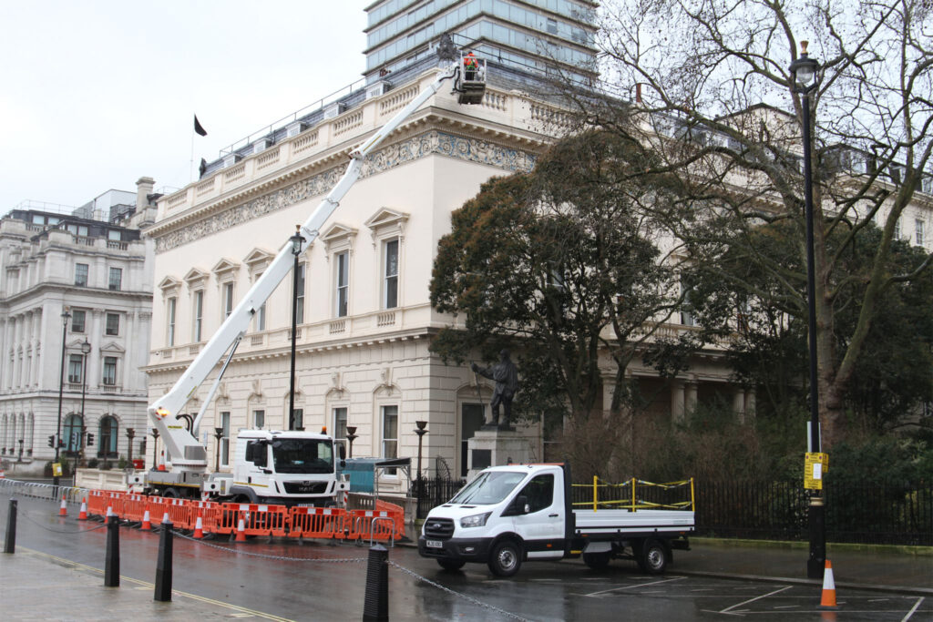 Styles Façade Solutions® deploy their specialist truck-mounted boom lift to conduct a comprehensive high-level façade survey on a grand Neoclassical property in central London. A fully PPE-equipped operative accesses the ornate upper façade and decorative roofline frieze from the elevated platform basket, with full traffic management in place below.