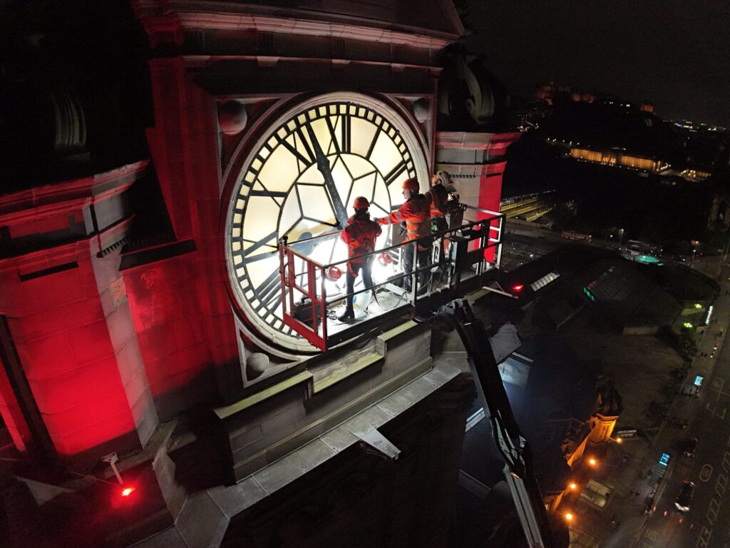 Night-time façade survey of The Balmoral Hotel in Edinburgh. The surveying team from Styles Façade Solutions (formerly Thomann-Hanry®) using a MEWP to undertake a commercial building façade survey, inspecting masonry and exterior stonework as part of a building condition survey for The Balmoral Hotel, Edinburgh.