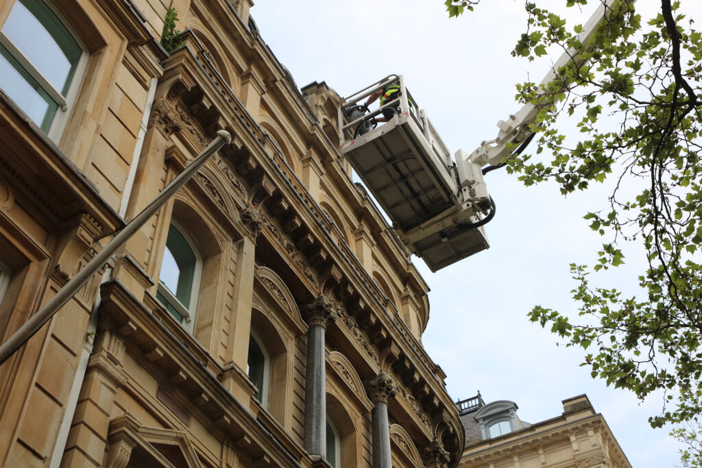 Styles Façade Solutions® operates a truck-mounted platform with a fully certified, trained IPAF operator, reaching high above street level to closely inspect ornate sandstone façade detailing. The elevated cradle provides precise, scaffold-free access to carved cornices and upper-storey stonework on this heritage building.