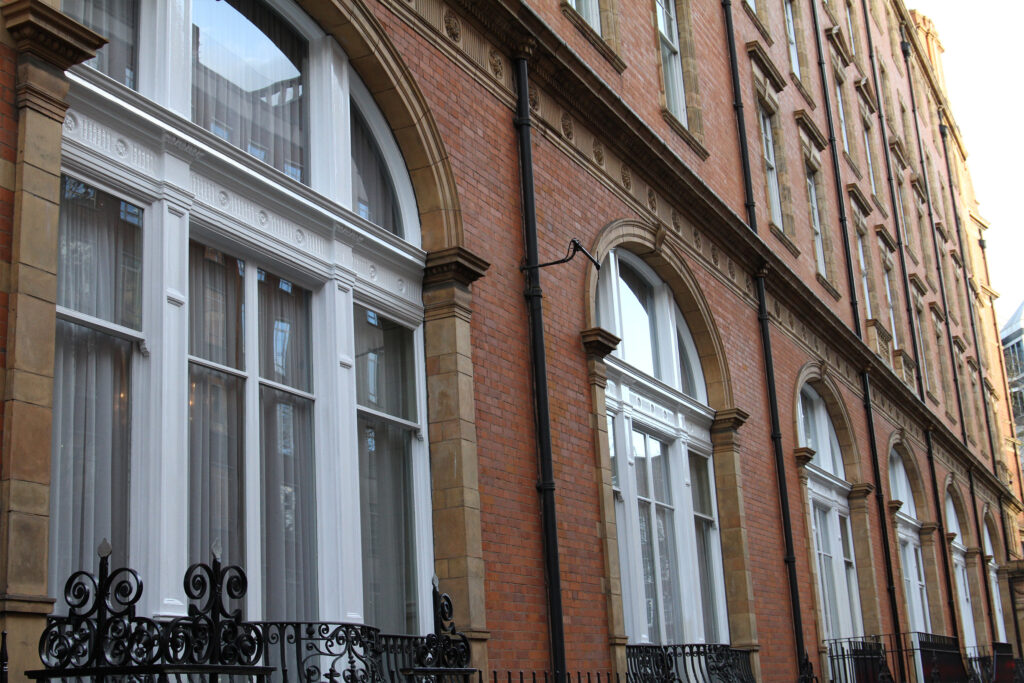 Styles Façade Solutions® completed the restoration and repainting of these sash windows at The Landmark Hotel, achieving a crisp white finish against the red-brick façade. The qualified painting team's work highlights the building's ornate arched window surrounds and decorative stonework detailing.