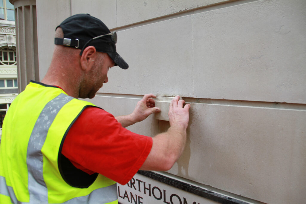 Styles Façade Solutions® carries out detailed stone repair to the Grade I listed Bank of England. Our stonemason carefully fits a Portland stone piece into the masonry on Bartholomew Lane, demonstrating precise, hands-on conservation work to preserve the historic façade.