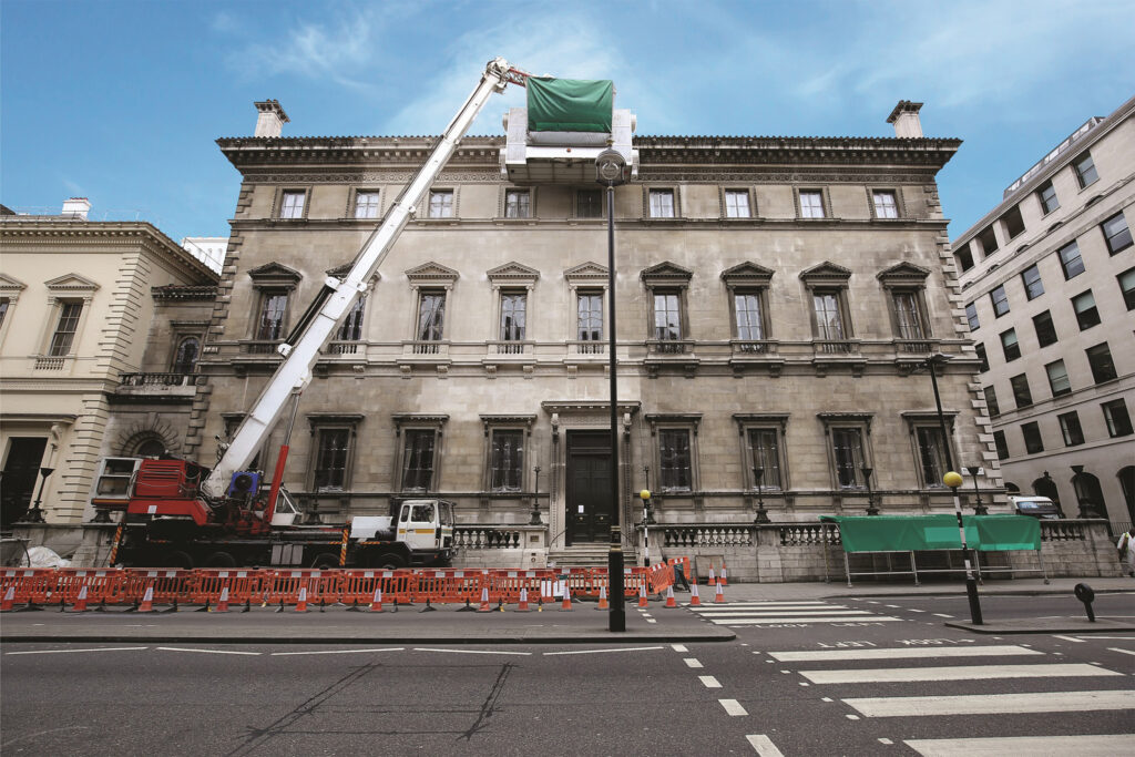 Styles Façade Solutions® uses a truck-mounted telescopic cleaning cabin to access the upper façade of the Reform Club, London. The striking contrast between freshly cleaned pale stonework and the still-soiled lower storeys, demonstrating the effectiveness of the scaffold-free Façade Gommage process.