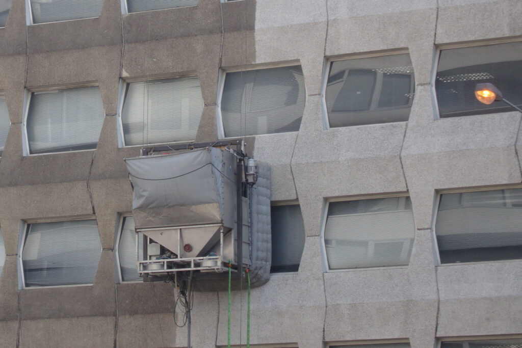 Styles Façade Solutions® showcases precast concrete, a durable structural material among the most common façade materials on commercial high-rises. This image shows specialist cleaning in progress via a suspended cradle, revealing the striking contrast restoration brings to weathered geometric concrete panelling.