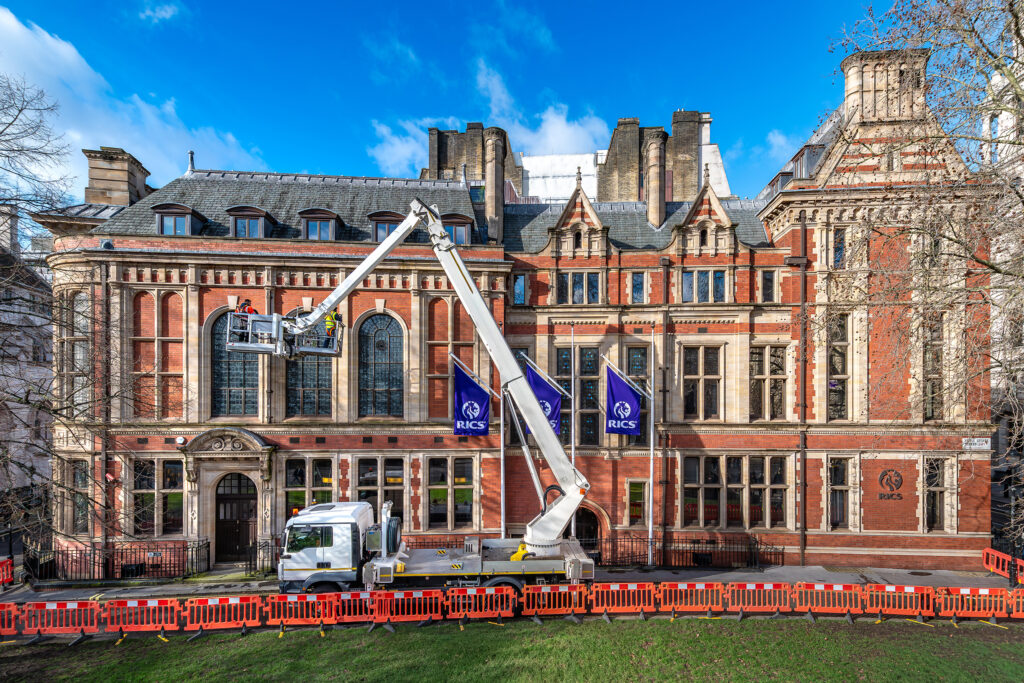 Styles Façade Solutions® conducts a detailed façade survey at Surveyors House, RICS headquarters in London. Technicians in a MEWP inspect the building's ornate red-brick and stone Victorian Gothic exterior, carefully examining windows and stonework to assess condition and guide future restoration and maintenance work.