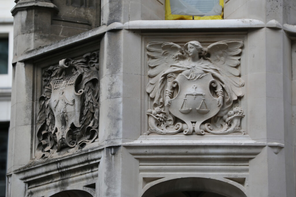 Styles Façade Solutions® demonstrating the effectiveness of dry, non-abrasive Façade Gommage cleaning at 13-15 Moorgate. The striking contrast between the soiled heraldic panel and freshly cleaned winged figure holding scales reveals intricate carved detailing, showcasing careful conservation that restores stonework without damaging delicate sculptural surfaces.
