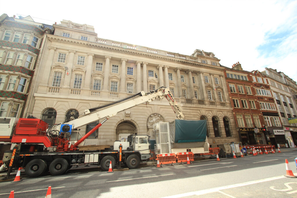 Styles Façade Solutions® carrying out sensitive heritage cleaning and restoration of the Grade II listed Apex Temple Court Hotel's ornate Portland stone façade. Crane-mounted access equipment supports careful conservation work on the building's Corinthian pilasters and decorative parapet, preserving its historic character on this busy London street.