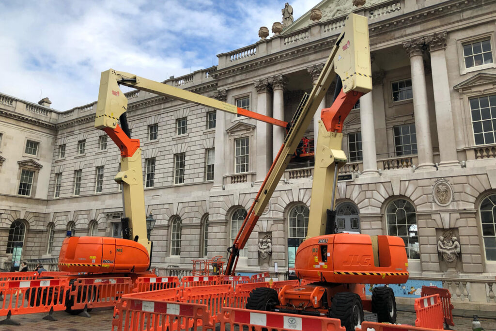 Styles Façade Solutions® carrying out stone masonry restoration on the Grade I listed Somerset House's Neoclassical Portland stone façade. Cherry picker boom lifts provide access to the ornate Corinthian columns and pediment sculptures, ensuring careful conservation of this historic courtyard's architectural heritage for future generations.