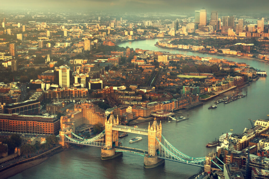 This sweeping aerial view captures London's architectural timeline in one frame; medieval Tower of London, Victorian Tower Bridge, Georgian and industrial-era warehouses lining the Thames, and Canary Wharf's contemporary skyline beyond. Illustrating almost two millennia of building styles converging along the capital's historic riverfront.